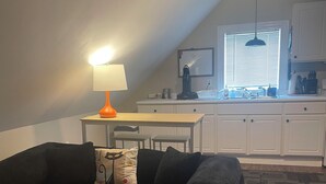 A compact living space with a sofa, a small table, a kitchen area with a sink and cabinets, and a window with blinds. - Entire rental unit in Warren, Rhode Island Unit 3 (Warren)