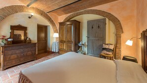 Een slaapkamer met een groot bed, een houten dressoir, een gewelfd bakstenen plafond en een kledingkast.