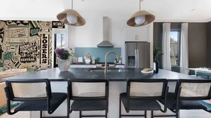 A modern kitchen with a central island, pendant lights, and a backsplash with vintage-style graphics.