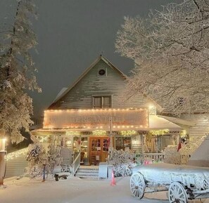 Een gebouw met sneeuw, een veranda, een koets en een bord met de tekst 'The American Inn'.