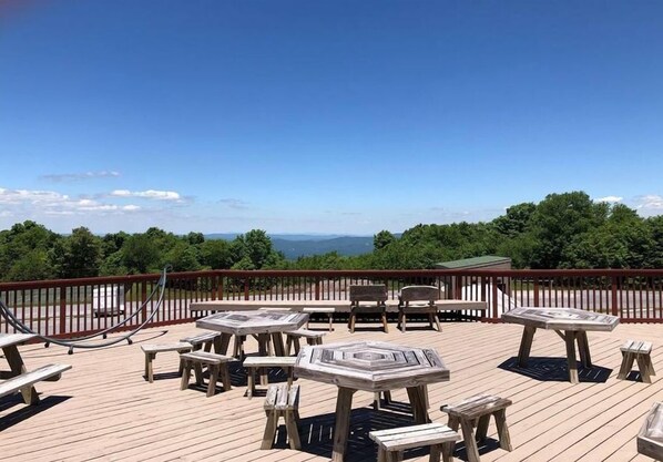 A wooden deck with picnic tables and chairs, overlooking a scenic landscape.