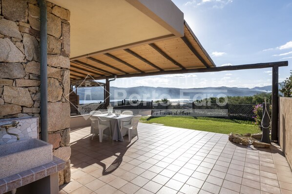 A covered patio with a stone wall, a grill, and a table with chairs.