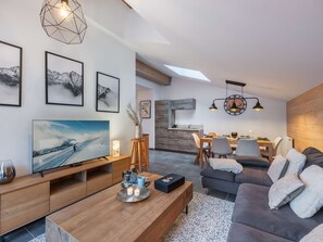 A modern living room with a flat-screen TV, wooden furniture, a dining area with a wooden table and chairs, and a kitchen with a wooden countertop. - APARTMENT CHÂTEL - Les Freinets A202 (CHATEL)