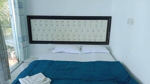 Hotellihuone, jossa on sänky, valkoiset vuodevaatteet, sininen peitto ja pääty.