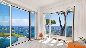 A modern room with large glass doors leading to a balcony with a view of the sea and boats. - Villa Nerea - by Elite Villas (Massa Lubrense)