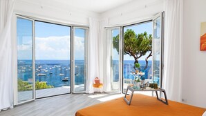 A bedroom with a large bed, a view of the sea, and a dining area with a table and chairs. - Villa Nerea - by Elite Villas (Massa Lubrense)