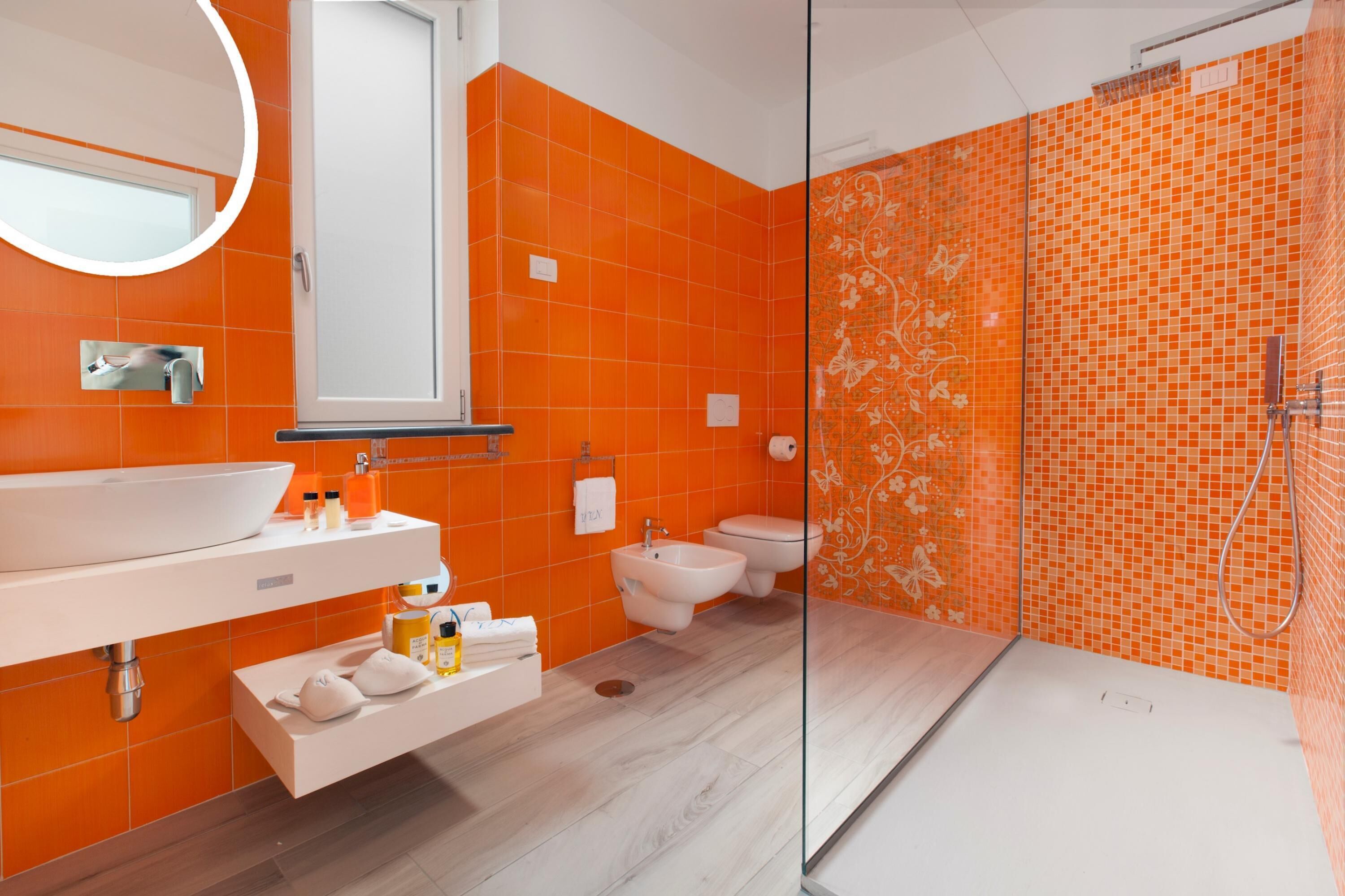 Ett modernt badrum med en stor, vit tvättställ, en dusch med glasväggar och orange kakel på väggarna.