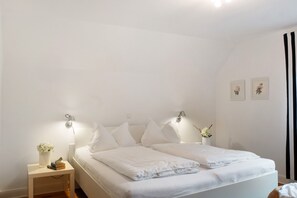 Un dormitorio con cama, mesitas de noche, lámparas de pared y un pequeño florero con flores.