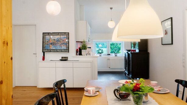 A modern kitchen with white cabinets, a dining table with chairs, and pendant lighting.