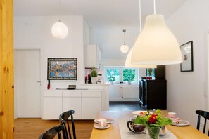 Una cocina moderna con armarios blancos, una mesa de comedor con sillas e iluminación colgante.
