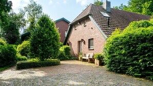 A brick house with a paved courtyard, a bench, and well-maintained hedges.