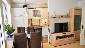 Une cuisine moderne avec des meubles blancs, un coin repas avec des chaises marron et un meuble de rangement en bois intégrant un téléviseur.