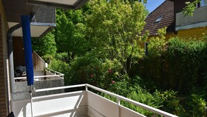 Un balcon donnant sur un jardin, avec une balustrade blanche et un tuyau bleu.