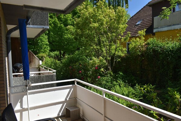 A balcony with a view of a garden, a white railing, and a blue pipe.