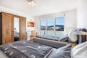 Ein Schlafzimmer mit zwei Betten, einem Holzschrank, einem Sessel, einem Schreibtisch und einem Fenster mit Blick.