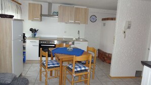 Una cocina compacta con estufa, horno y lavaplatos. Hay una mesa de comedor con sillas y un reloj en la pared.