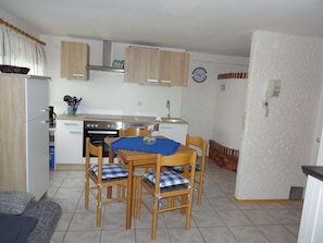 A compact kitchen with a stove, oven, and sink. There is a dining table with chairs and a clock on the wall.
