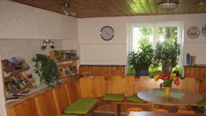 Una cocina con armarios de madera, una mesa de comedor con sillas, un reloj y plantas en macetas.