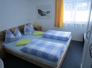 Un lit double avec une literie à carreaux bleus et blancs, une tête de lit en bois et une petite table de chevet avec une lampe.
