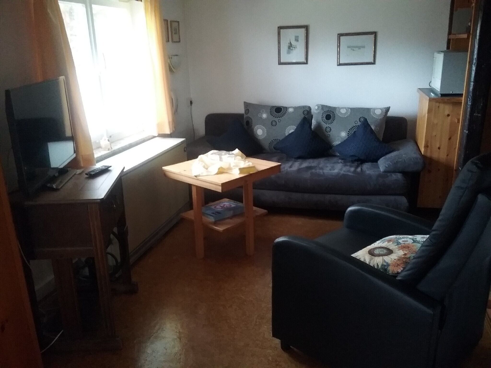 Un salon avec un canapé, un fauteuil, une petite table, un téléviseur et une fenêtre.