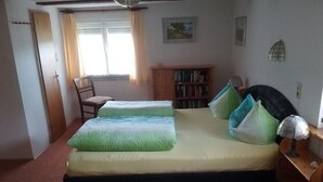 Un dormitorio con cama, una silla, estantería y ventana.