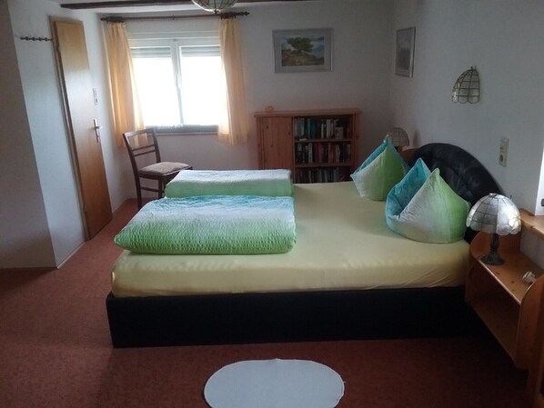 Ein Schlafzimmer mit Bett, Stuhl, Bücherregal und Fenster.