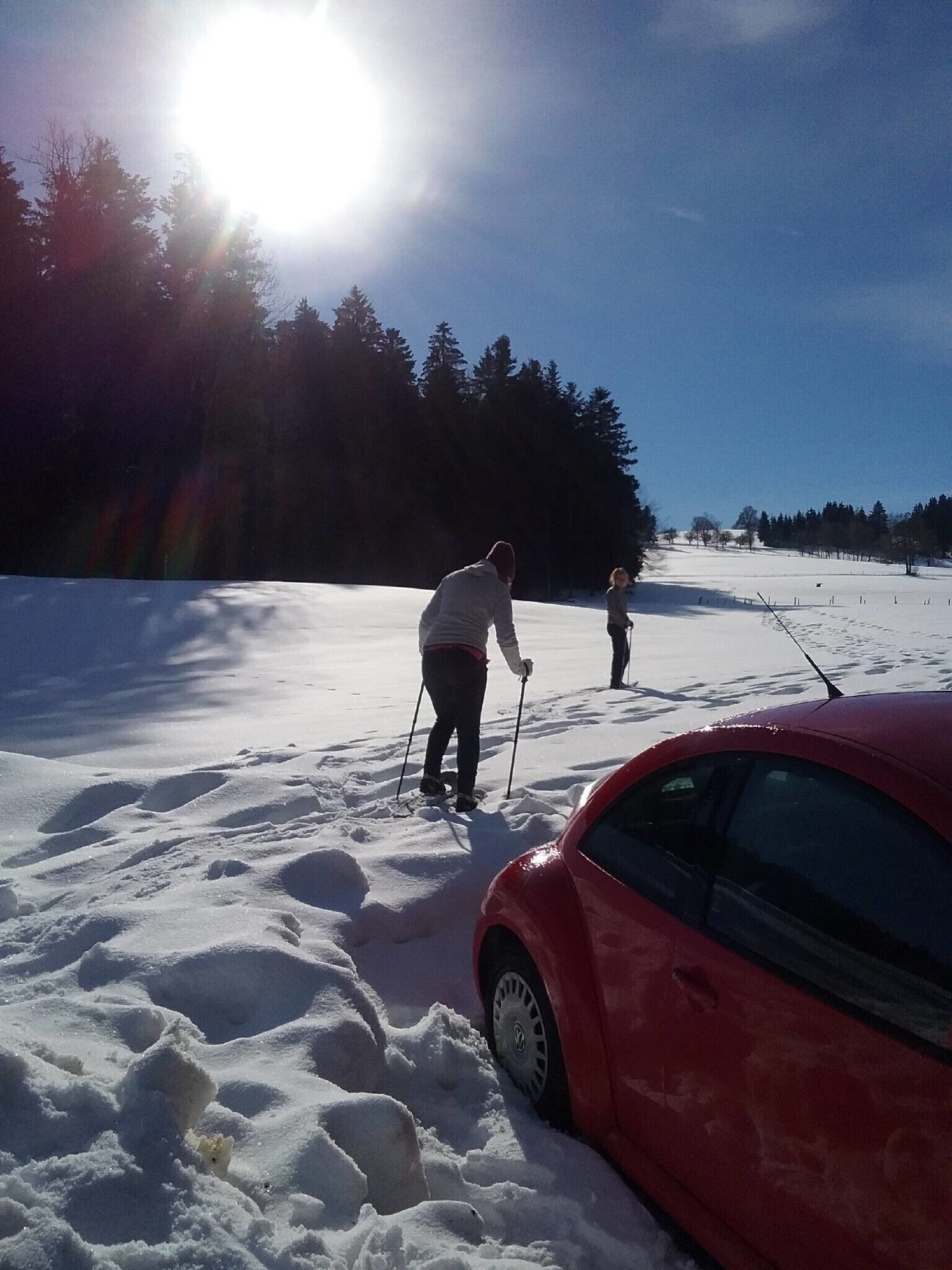 Lumipeitteinen maisema, jossa oikealla puolella on punainen auto, etualalla hiihtäjä ja taivaalla ei ole pilviä.