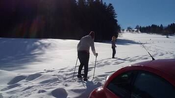 Lumipeitteinen maisema, jossa oikealla puolella on punainen auto, etualalla hiihtäjä ja taivaalla ei ole pilviä.