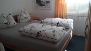 Un letto con cuscini a motivi floreali, un comodino, un quadro incorniciato appeso al muro e una finestra con tende.