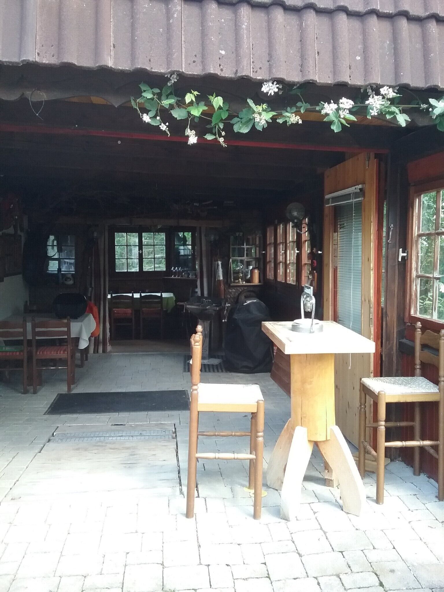Een terras met houten stoelen en tafels, een barbecue en een overdekte veranda.