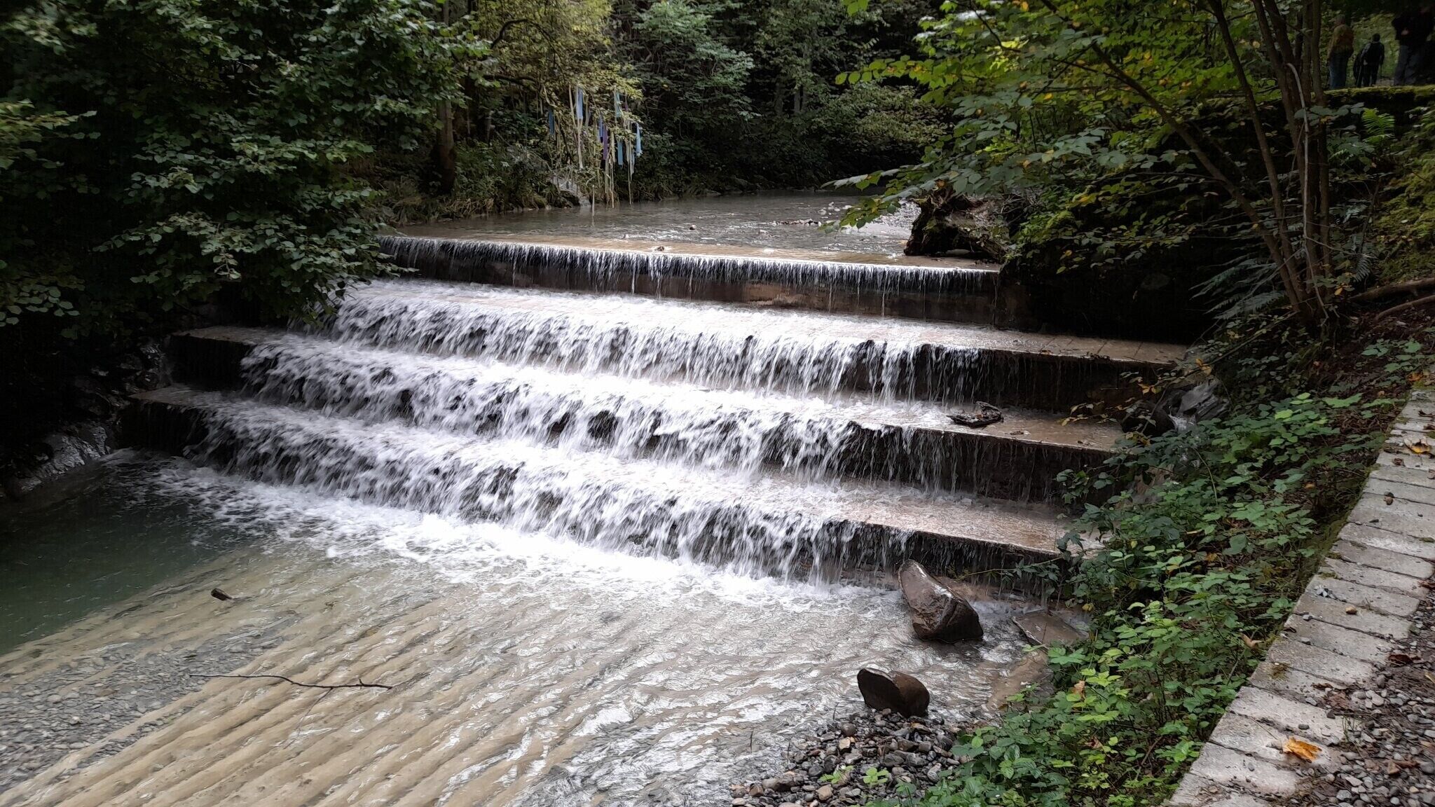 Una cascada escalonada en un área boscosa con un sendero de piedra.