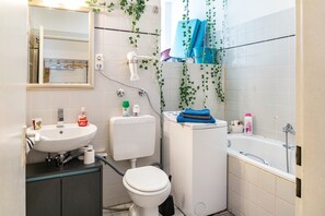 Une salle de bain comprenant un lavabo, des toilettes et une baignoire, avec un miroir au-dessus du lavabo et un porte-serviettes au-dessus de la baignoire.