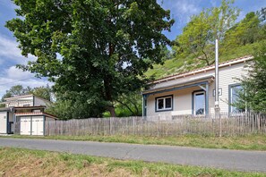 A residential house with a wooden fence, a garage, and a large tree in front. - Holiday Home "Ferienhaus Das Kleine Paradies" with Sauna, Garden and Wi-Fi (Liebenau)
