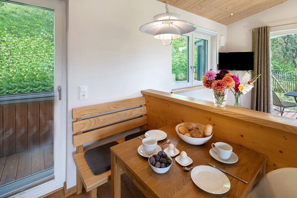 Una mesa de madera para comer con platos, tazas y un cuenco de fruta. Un banco se encuentra junto a la mesa.