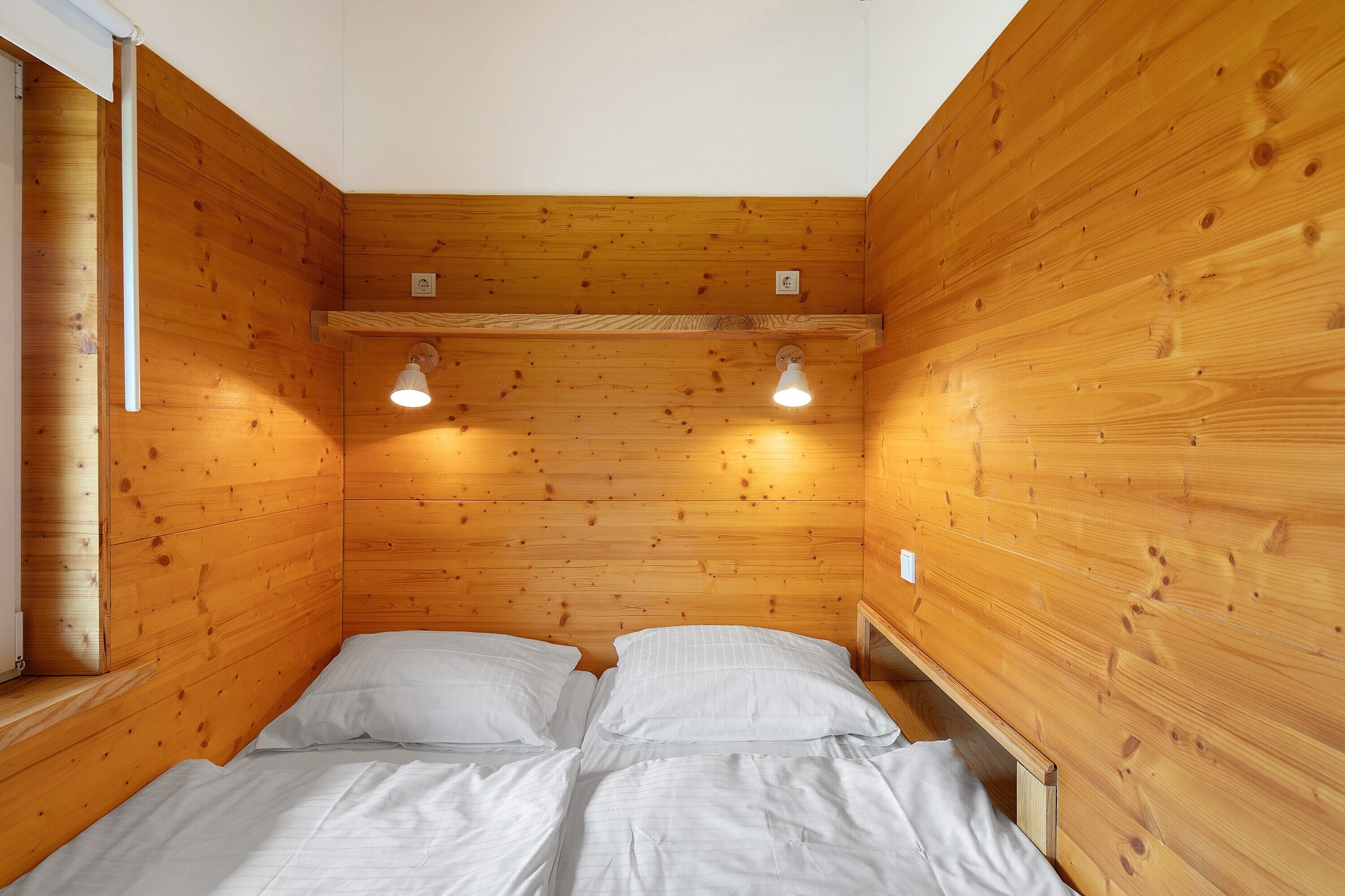 Een kamer met houten lambrisering, een bed, twee wandlampen en een raam.