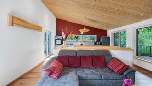 A modern living room with a grey sectional sofa, a wooden ceiling, and large windows.