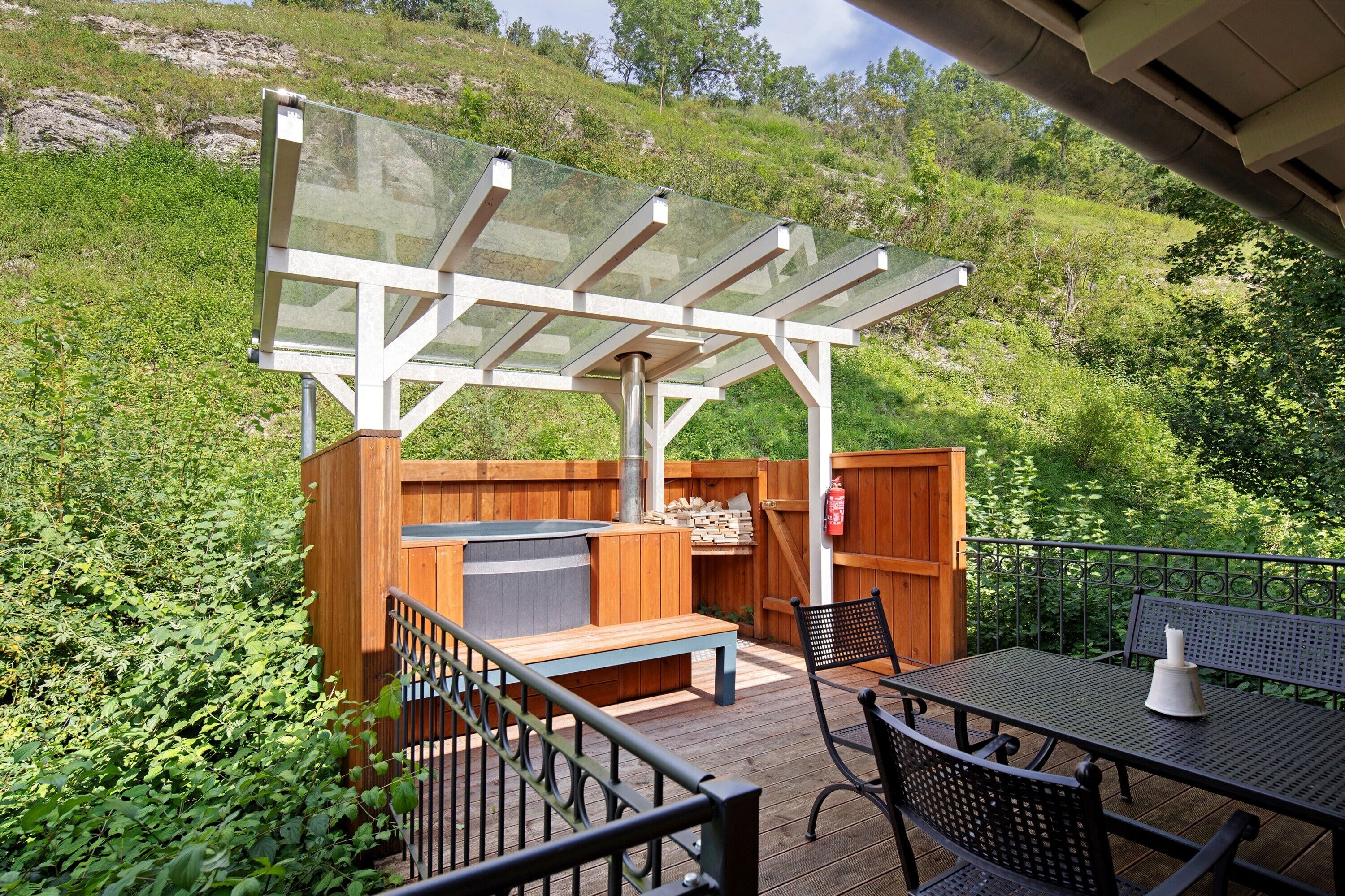 A patio with a wooden deck, a glass enclosure, a barbecue area, and outdoor furniture.