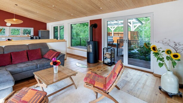 A modern living room with a sofa, coffee table, and chairs, a fireplace, and large windows offering a view of the outdoors.