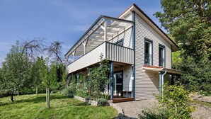 A two-story house with a balcony, surrounded by greenery.