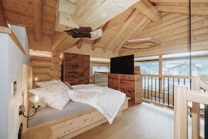 L’intérieur d’un chalet en bois comprend un lit, un téléviseur fixé au mur et un balcon doté d’une balustrade.