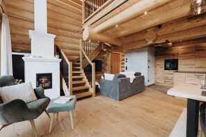 Een houten interieur met een open haard, een bank, een eettafel en een keukenhoek.