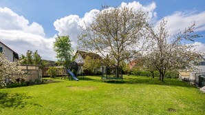A grassy backyard with a playground, a tree, and a house in the background. - Apartment 'Friedmann' with Private Garden, Balcony and Wi-Fi (Offingen)