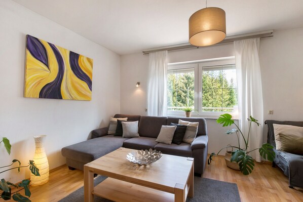 A modern living room with a sofa, a coffee table, a painting, and a window with curtains.