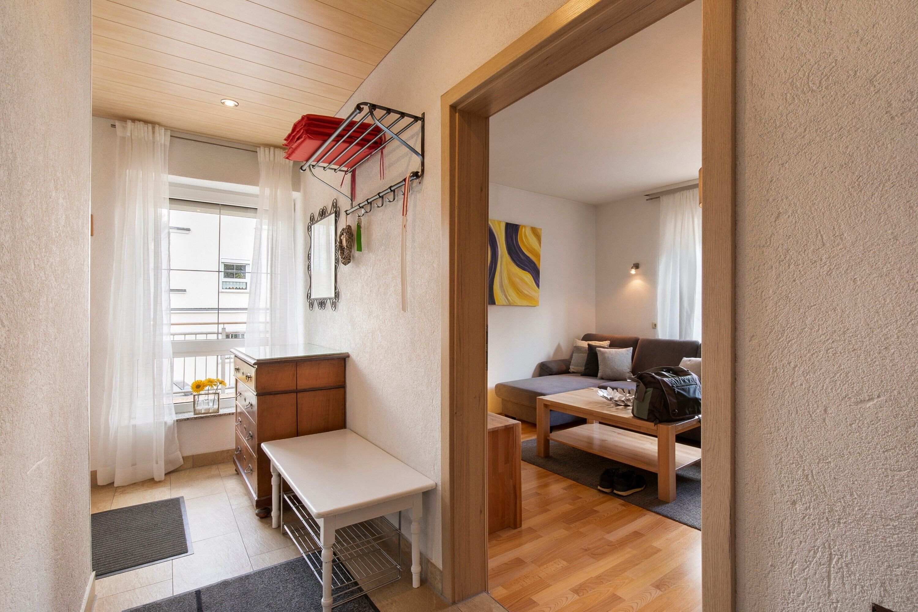 Een knus kamertje met een houten plafond, een tafeltje, een bankje, een bank en een wandrek voor wasgoed.