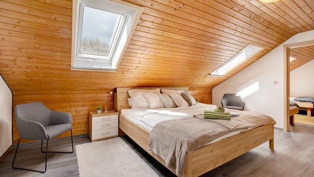 A bedroom with a wooden ceiling, a bed, a chair, a nightstand, and a window. - Apartment 'Friedmann' with Private Garden, Balcony and Wi-Fi (Offingen)