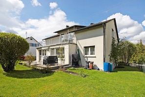 A two-story house with a balcony, a lawn, and a garden.