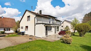 Ein zweistöckiges Haus mit Balkon, gepflasterter Auffahrt und einem gepflegten Rasen.