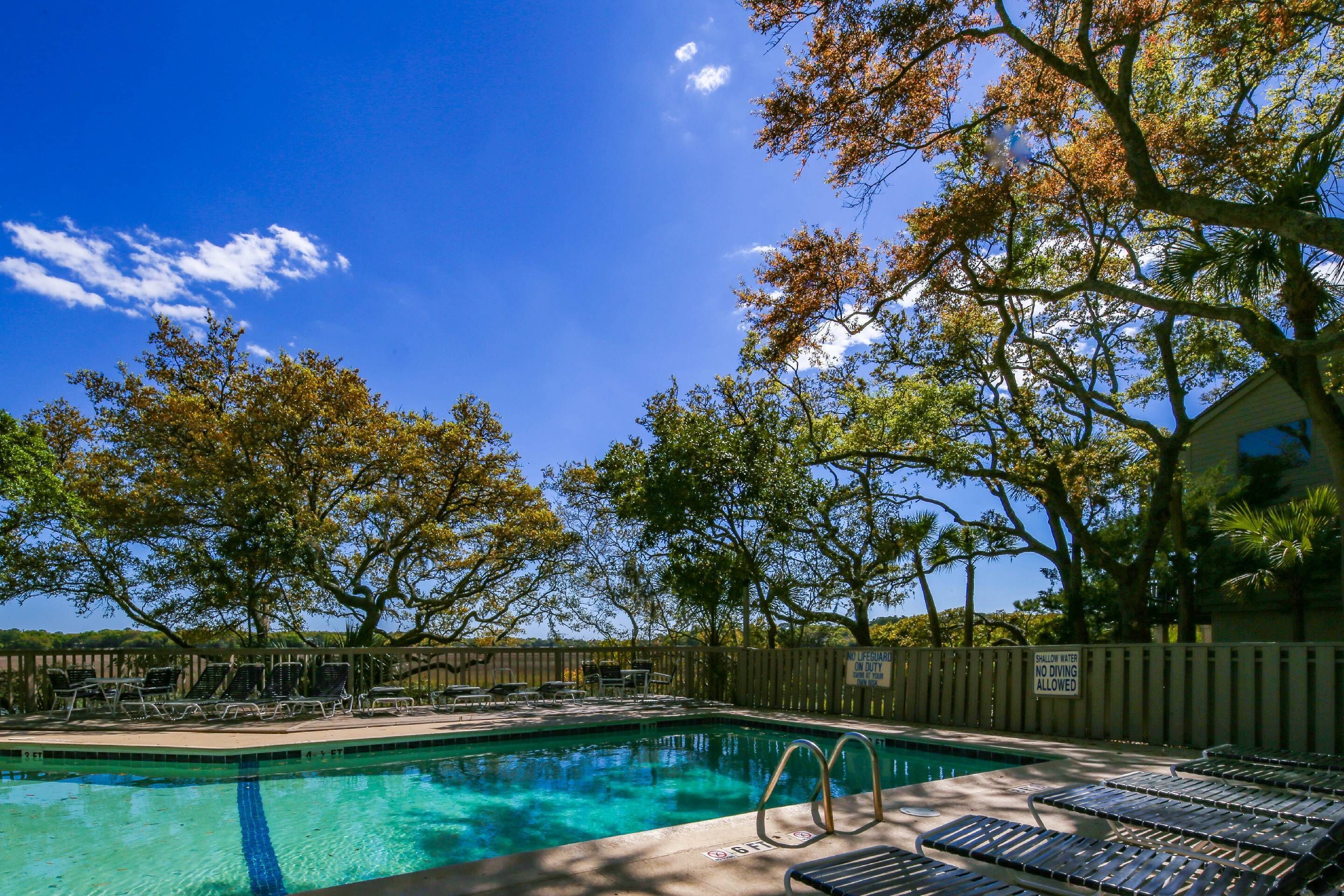A clear blue pool with lounge chairs and a wooden fence.