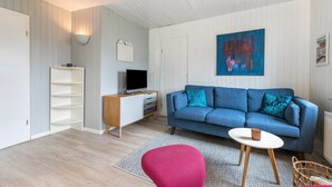 Un salon moderne avec un canapé bleu, un fauteuil rouge, une petite table blanche et un tableau accroché au mur.