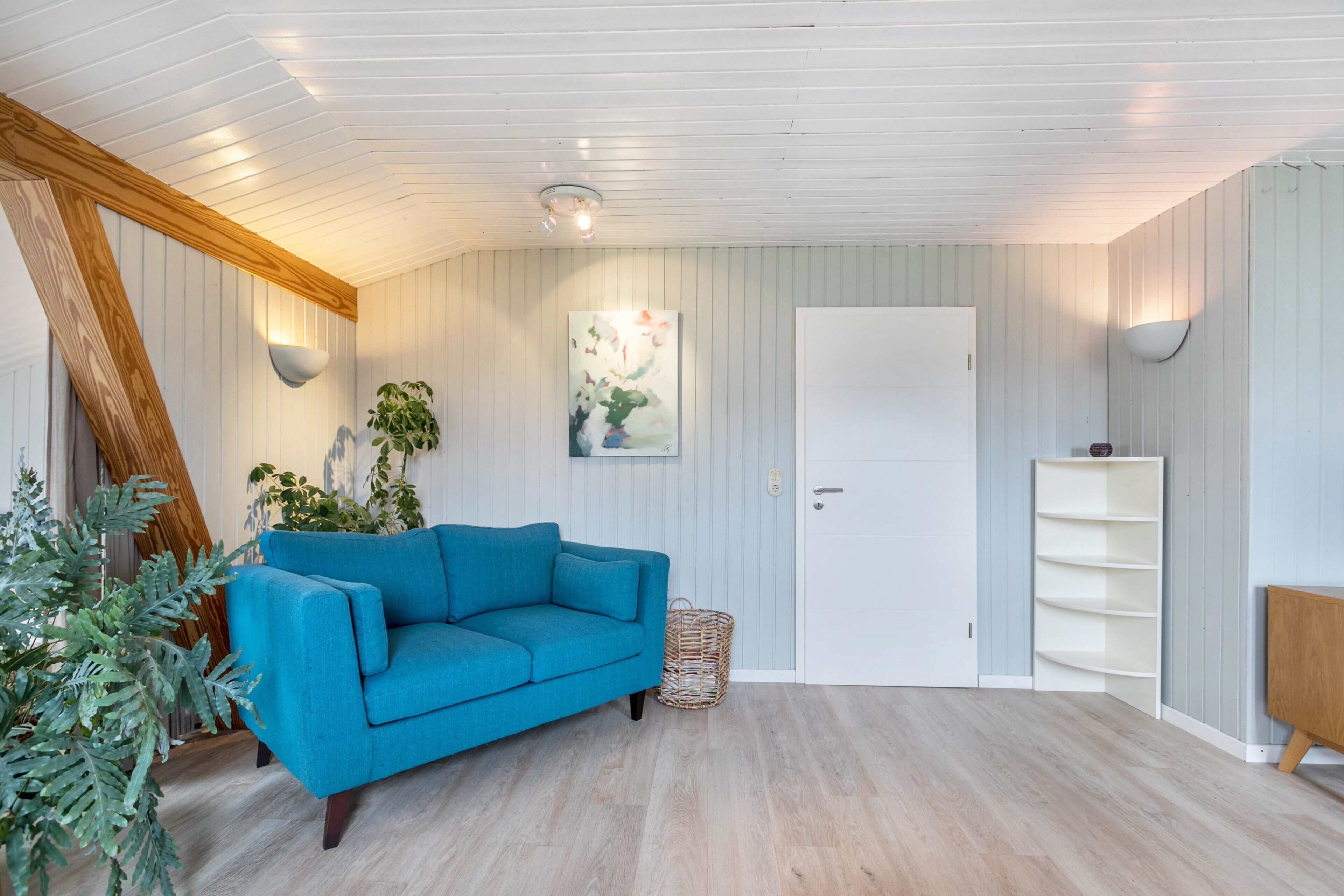 A room with a blue sofa, a white door, and a wall-mounted shelf.